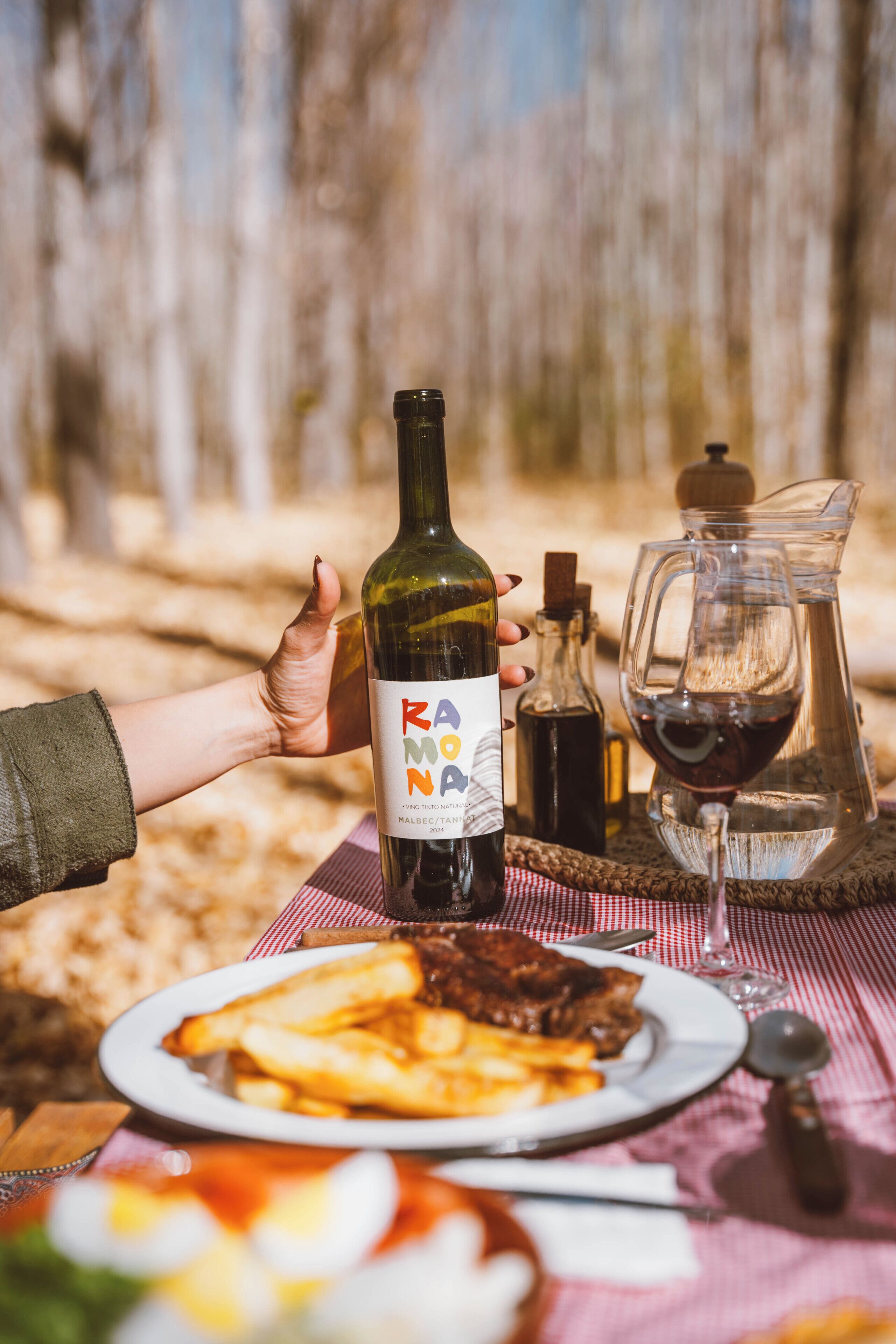 Una mesa con una botella de vino tinto, una jarras y un plato de comida.