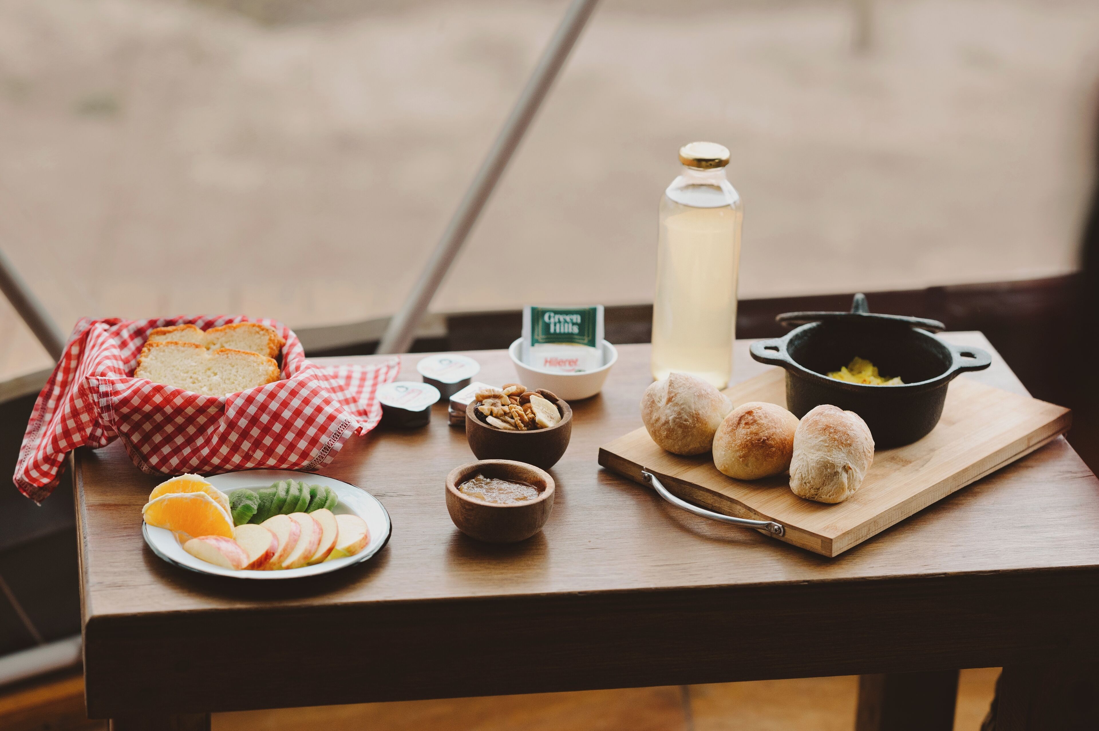 A wooden table with a variety of breakfast items including bread, fruit, nuts, and a pot of eggs.