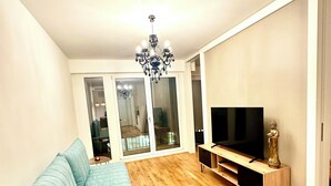A living room with a sofa, TV, wooden flooring, and a chandelier. - Most popular apartment in the center (Dresden)