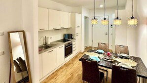 A modern kitchen with white cabinets, a dining table set for four, and a hanging light fixture above. - Most popular apartment in the center (Dresden)