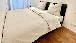 A modern bedroom with a large bed, white bedding, and a wooden floor. - Most popular apartment in the center (Dresden)