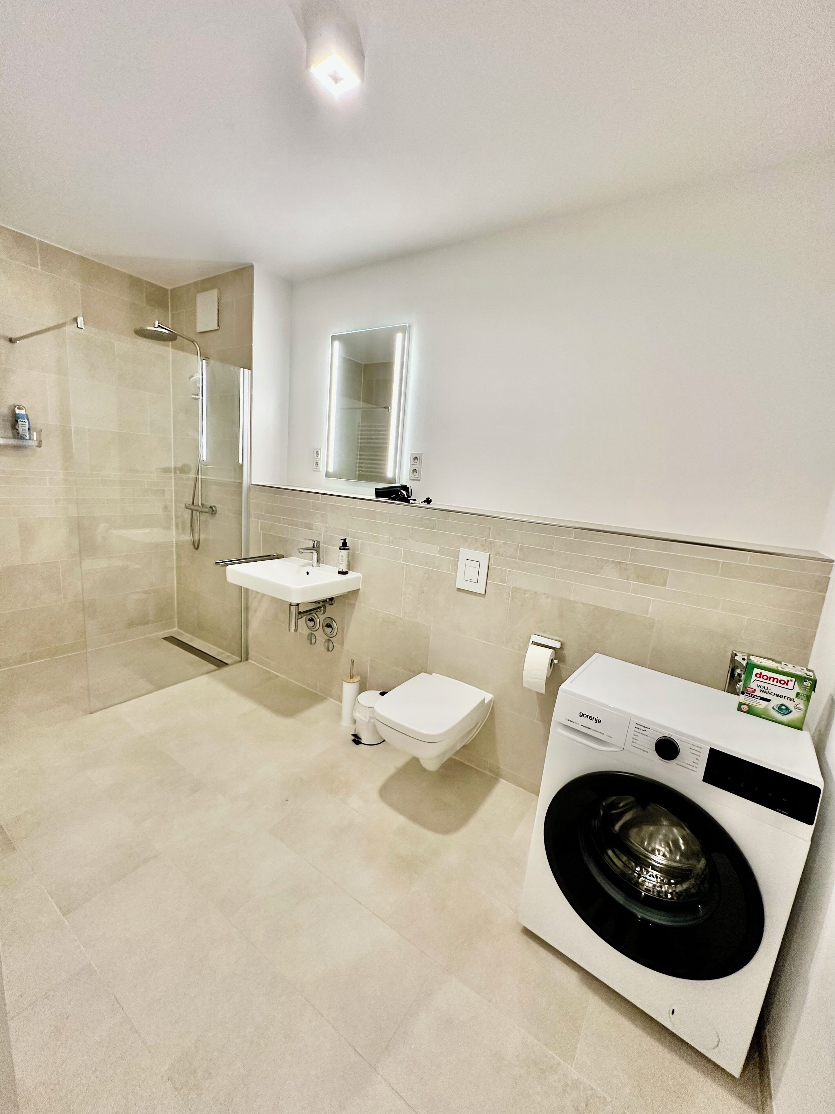 Ein modernes Badezimmer mit einer Duschkabine, einem Waschbecken, einer Toilette und einer Frontlader-Waschmaschine.