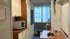 A compact kitchen with a microwave, wooden cabinets, a dining table with chairs, and a hanging plant.