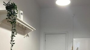 A small, clean room with a wooden table, white chairs, a refrigerator, and a hanging plant.