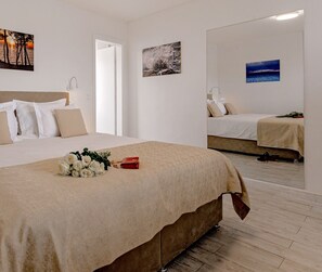 A hotel room with a large bed, a smaller bed, and a mirror reflecting the room. There are wall art pieces and a bouquet of flowers on the bed. - Villa Zvonko (Split)