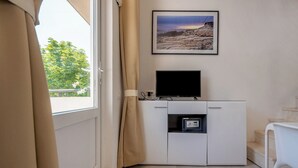 Une pièce avec un meuble blanc, un téléviseur à écran plat, un tableau encadré au mur et une fenêtre avec des rideaux.