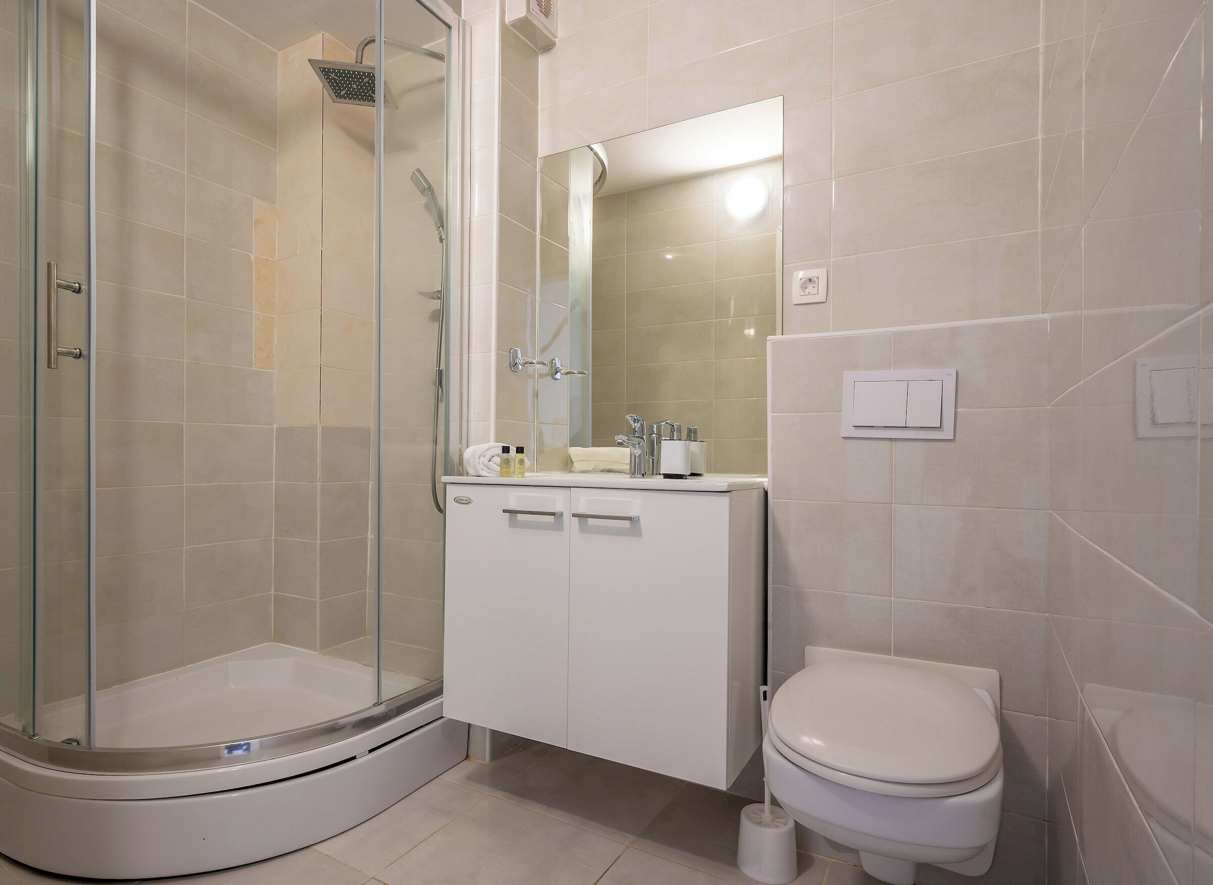 A modern bathroom with a glass-enclosed shower, a white sink with toiletries, and a toilet.