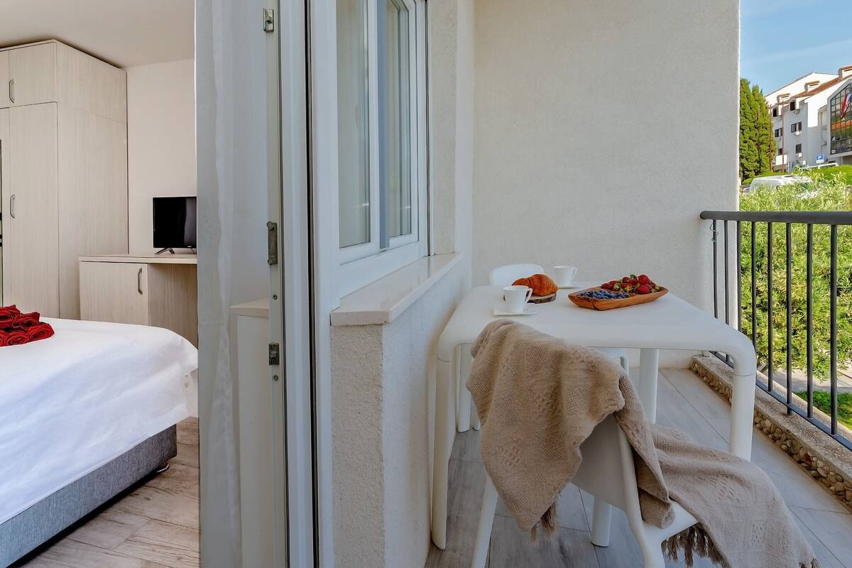 A balcony with a table set for breakfast, a bed, and a TV in a room.