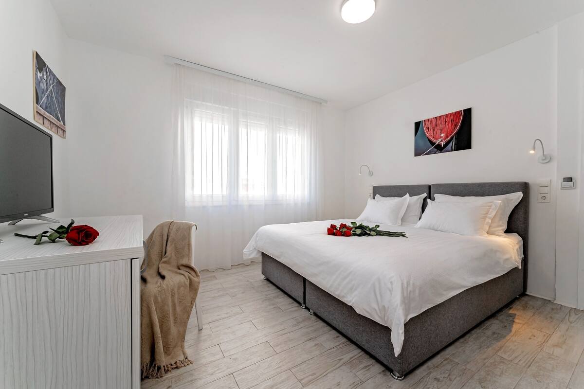 A bedroom with a bed, a TV, and a window with curtains.
