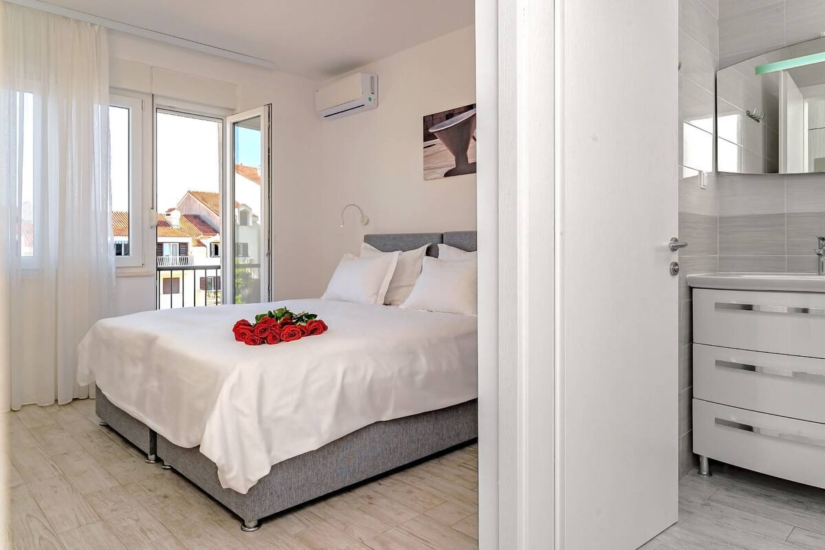 A bedroom with a bed, a bathroom with a sink, and a view of buildings outside.