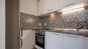 Une cuisine compacte dotée d’un four encastré, d’un évier et d’un pare-feu en carreaux.