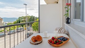 Un balcon avec une assiette sur laquelle on trouve un croissant, des fraises et des myrtilles, une tasse blanche et un vase rempli de fleurs.