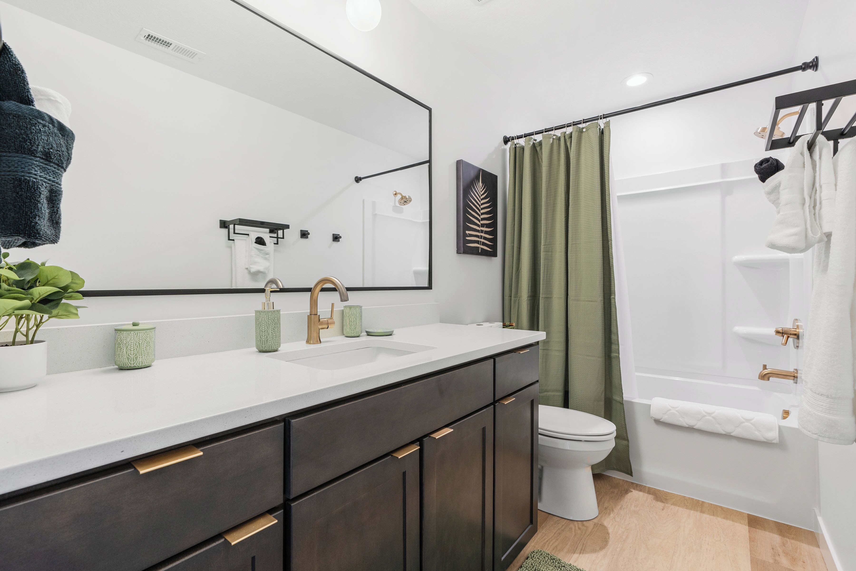 Une salle de bain moderne avec un lavabo blanc, des meubles sombres, un grand miroir, des toilettes et un espace douche.