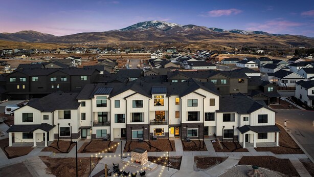 Ein moderner Wohnkomplex mit mehreren zweigeschossigen Häusern, einem zentralen Innenhof mit Außenbestuhlung und Blick auf die Berge.