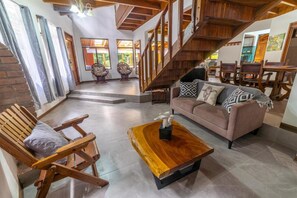 Ein geräumiger Wohnbereich mit einer Holztreppe, einem Sofa, einem Couchtisch und Korbstühlen.