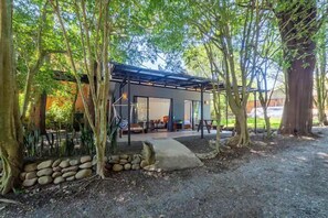 A modern outdoor seating area with a covered patio, surrounded by trees and a stone wall. - Violeta Homes Monteverde (Monteverde)