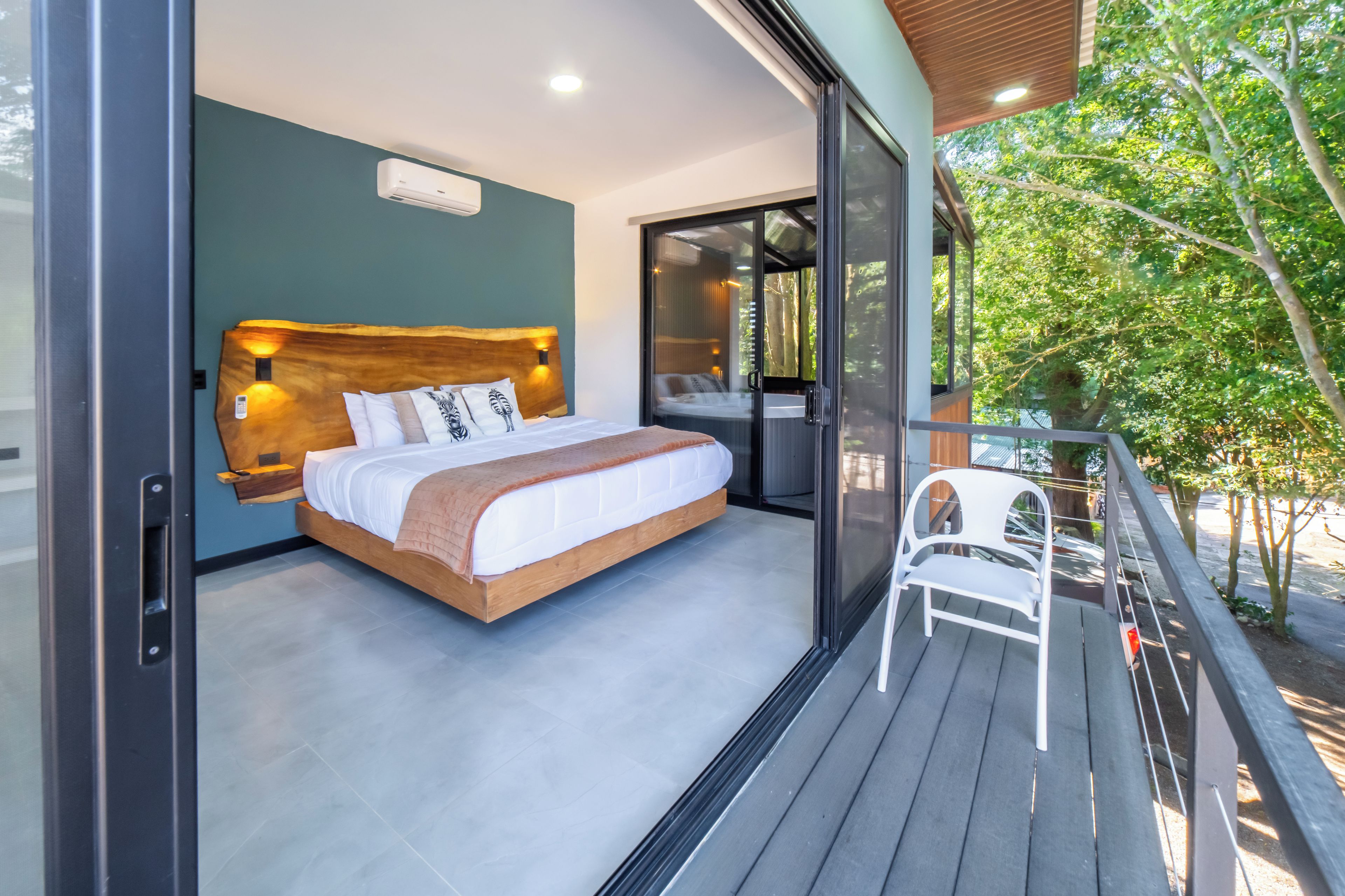 Une chambre moderne avec un grand lit, une tête de lit en bois et un balcon avec une chaise.