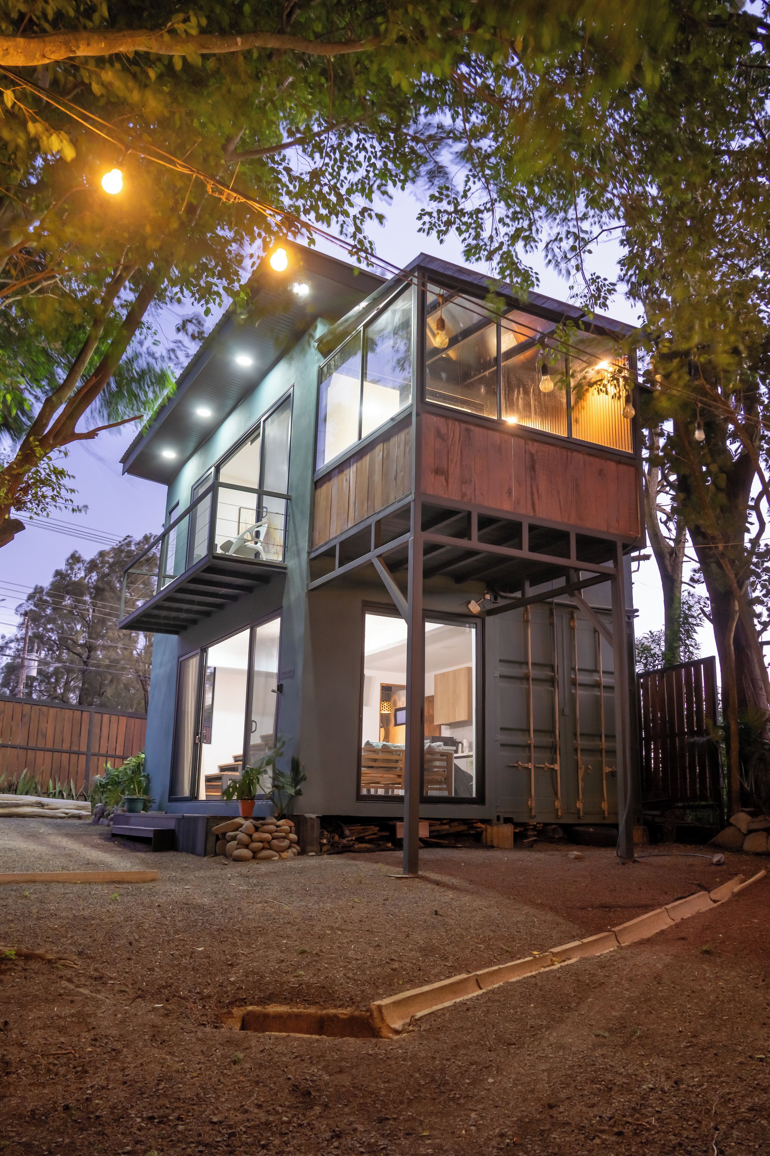Una casa de dos pisos con fachada de vidrio, terraza de madera y escalera de metal.