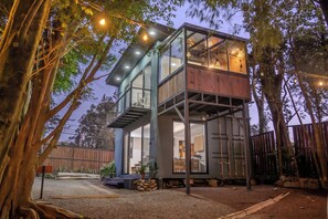 A two-story wooden cabin with a glass balcony, surrounded by trees and a gravel driveway. - Violeta Homes Monteverde (Monteverde)
