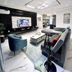 A modern living room with a large TV, a sofa, a coffee table, and a TV stand. - Somewhere Apartments (Abuja)
