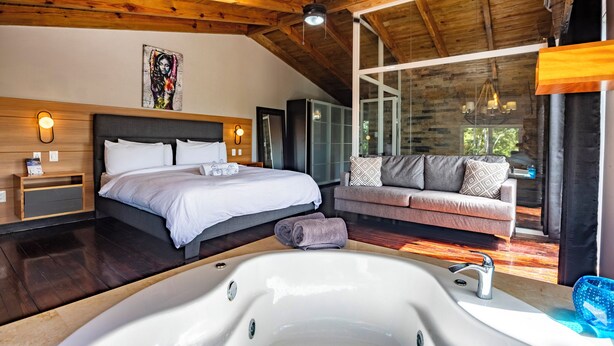 A modern bedroom with a large bed, a sofa, a bathtub, and a view of the outdoors. - Villa Twelve27 (Sosúa)