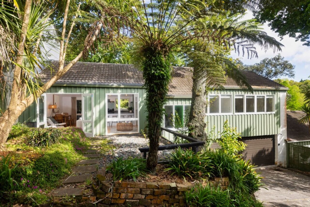 A green house with a porch, a small garden, and a garage.