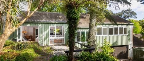 A green house with a porch, a small garden, and a garage.
