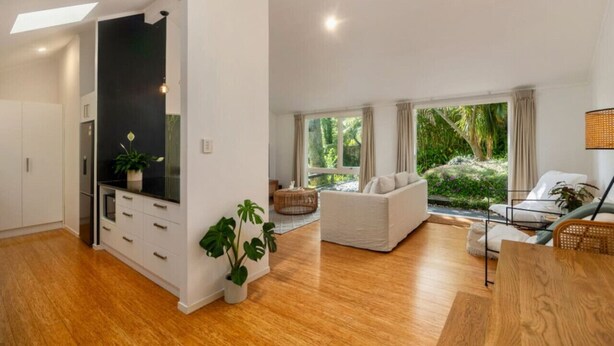 Una sala moderna con sofá, mesa de comedor y área de cocina con armarios blancos y encimera negra.