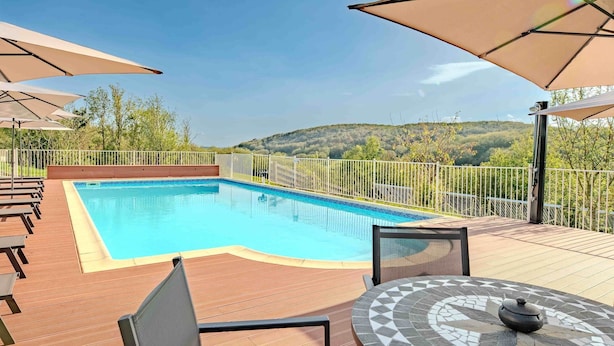 Ein Schwimmbecken mit Holzterrasse, Sitzgelegenheiten im Freien und Sonnenschirmen.