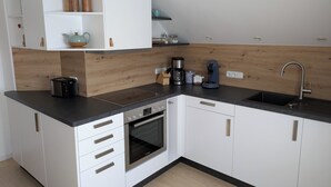 Une cuisine moderne avec des meubles blancs, un four encastré, une machine à café et un évier.