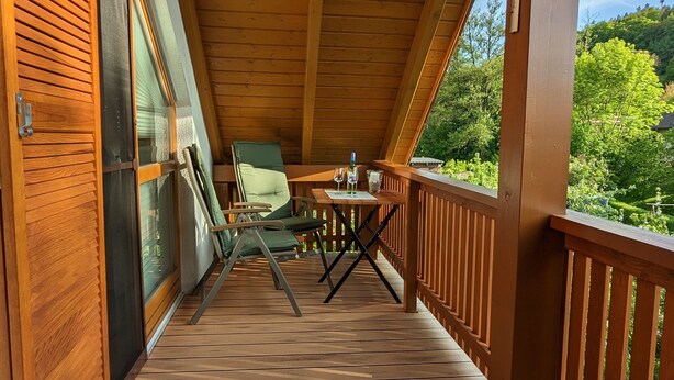 Une terrasse en bois avec une table et des chaises, donnant sur un paysage verdoyant.