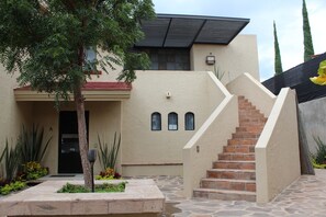 A building with a stone staircase leading to a door, surrounded by plants and a tree. - Modern Ajijic 1 Bdrm Home-walk To Everything -gym-pickleball Court-golf Cart (Chapala)