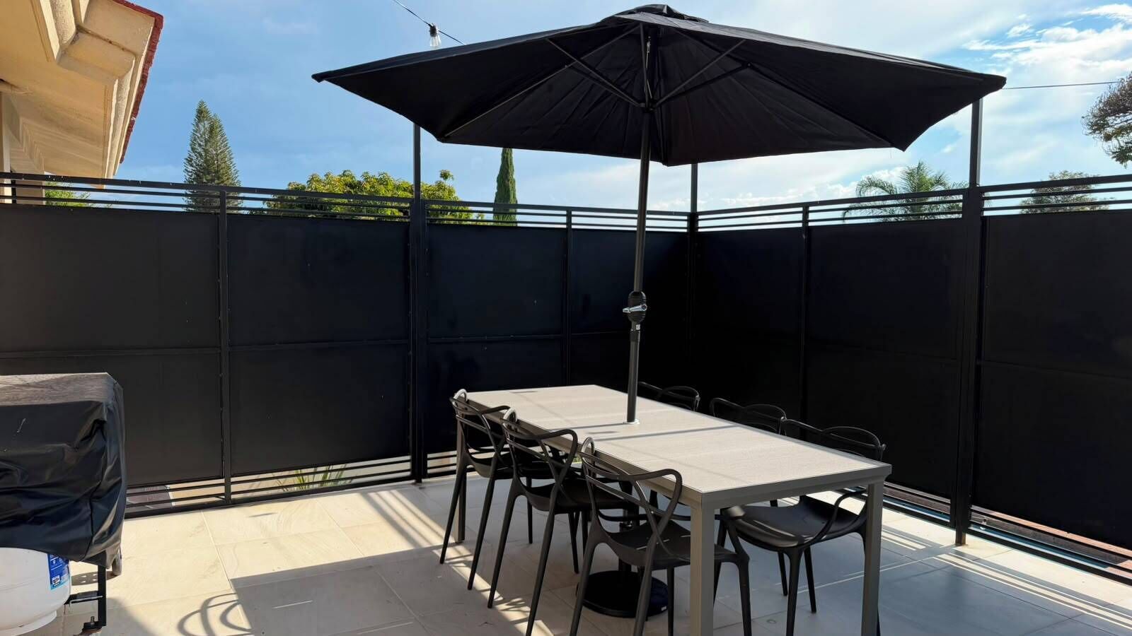 En udendørs terrasse med et bord, stole, grill og stor parasol.