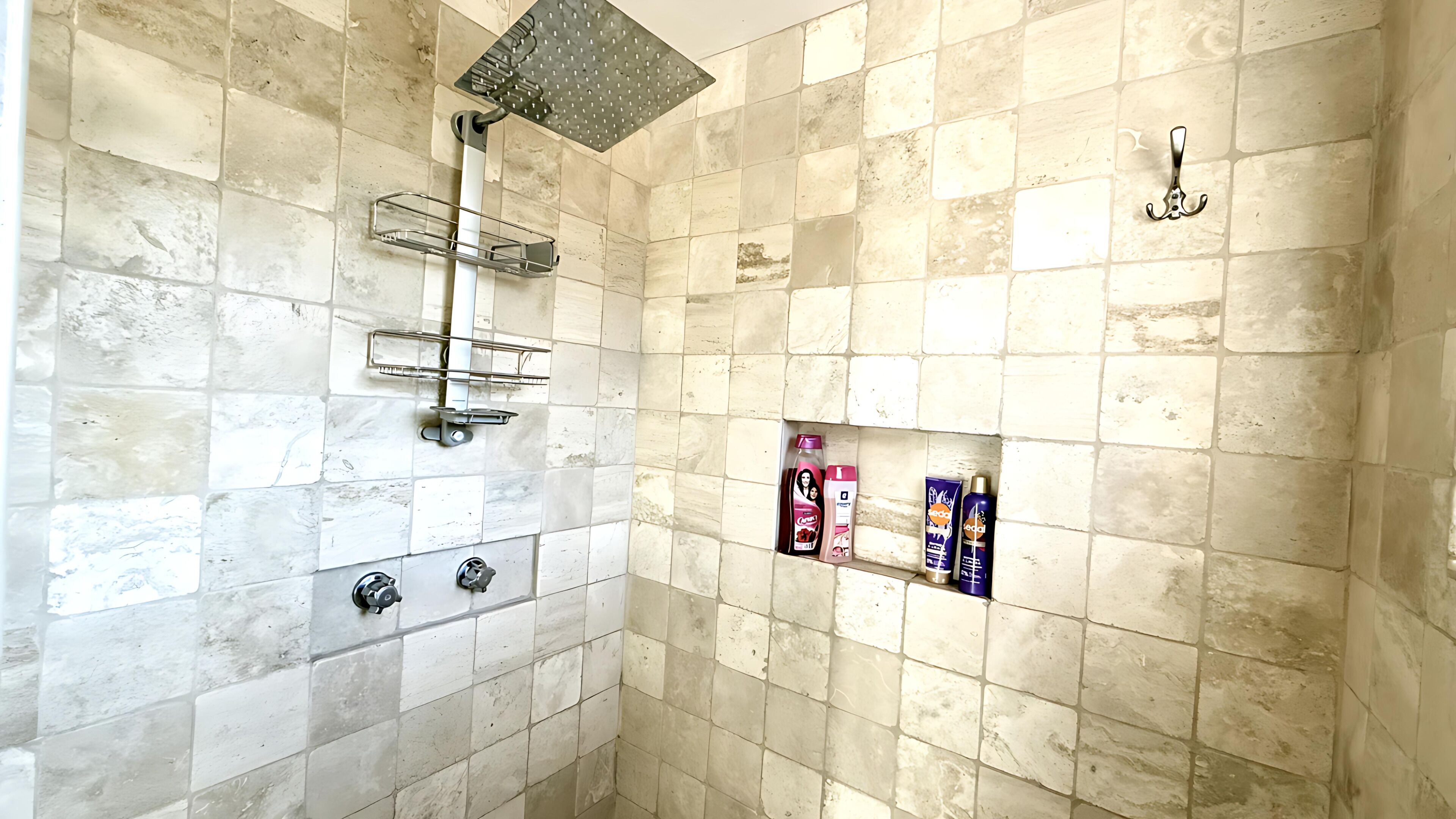 A bathroom with a tiled floor, a shower, and a shelf with toiletries.