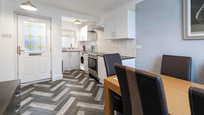 A modern kitchen with white cabinets, a dining area with a wooden table and chairs, and a patterned herringbone floor.
