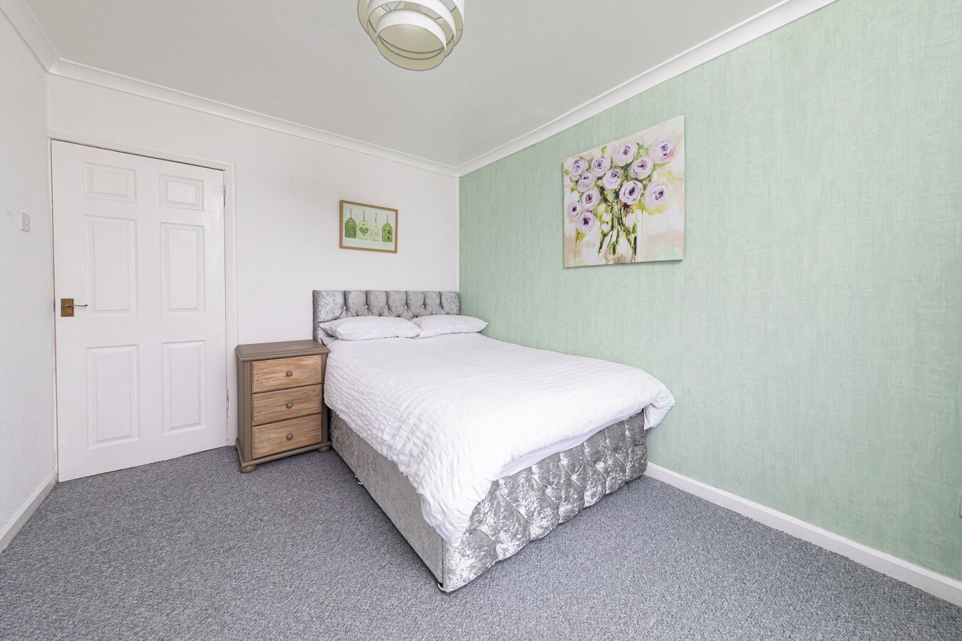Une chambre à coucher avec un lit, une table de chevet, une porte et un tableau au mur.