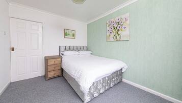 Une chambre à coucher avec un lit, une table de chevet, une porte et un tableau au mur.