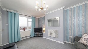 A living room with a TV, a sofa, a chandelier, and a window with curtains.