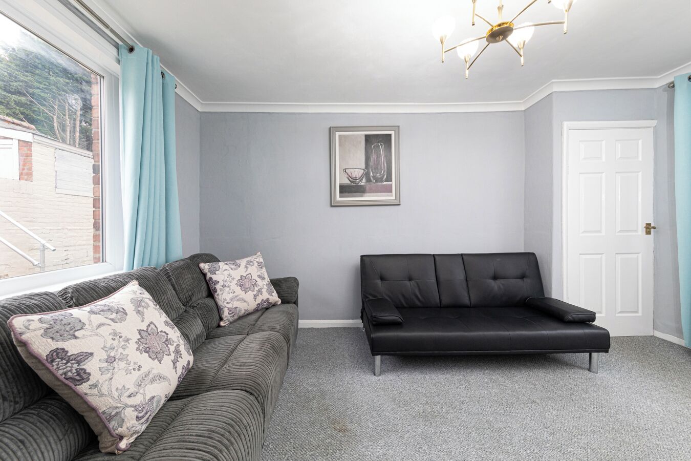 Ein Zimmer mit einem grauen Sofa, einem schwarzen Sofa und einem gerahmten Bild an der Wand.