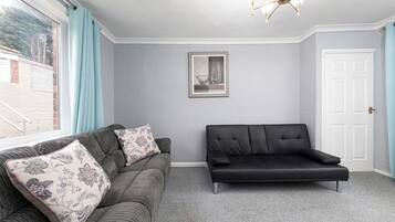 Ein Zimmer mit einem grauen Sofa, einem schwarzen Sofa und einem gerahmten Bild an der Wand.