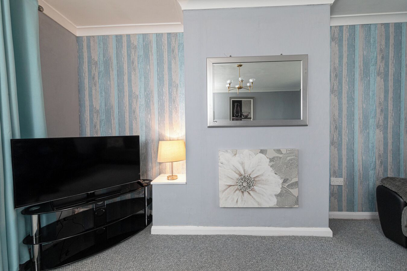A living room with a flat-screen TV, a lamp, a mirror, and a floral artwork on the wall.