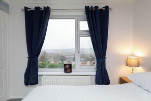 Quarto com cama, janela com cortinas, radiador, luminária e vista para o exterior.