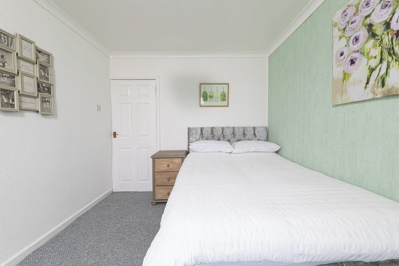 A bedroom with a bed, a dresser, a door, and a wall with framed pictures.
