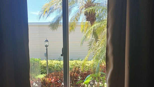 A room with a window overlooking a garden, a table with a striped tablecloth, and two glasses of a dark beverage. - Naples Florida Paradise - 2 week Min Stays (Naples)