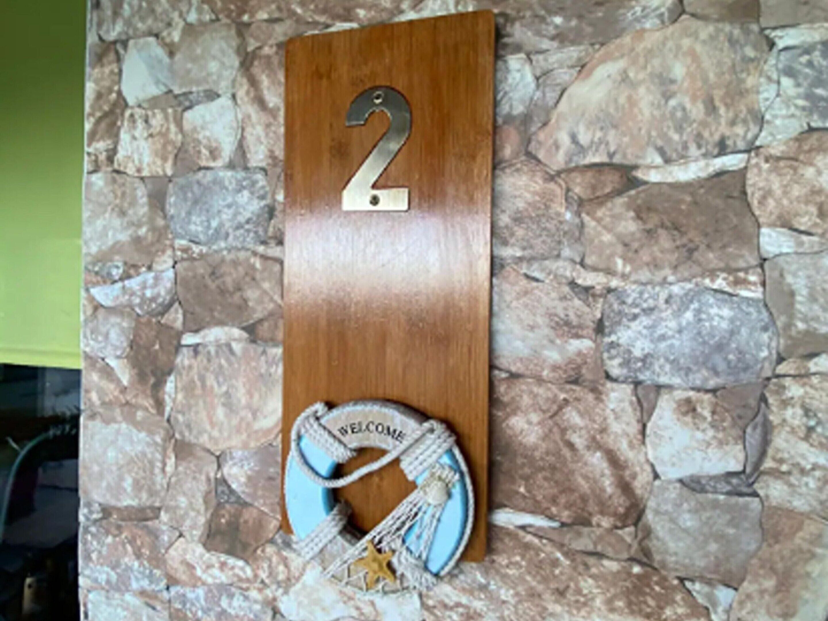 Un letrero de madera con el número 2, un felpudo y una decoración con forma de estrella en una pared de piedra.