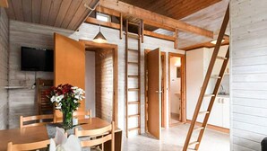 Un intérieur en bois comprenant un coin repas, un téléviseur fixé au mur et un escalier menant à un autre niveau.