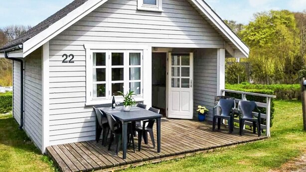 Une petite maison de plain-pied, avec le numéro « 22 » sur le côté, une véranda avec une table et des chaises, et une petite terrasse.