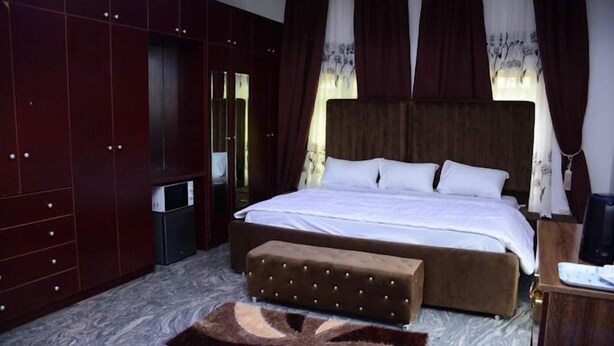 Een slaapkamer met een groot bed, een houten garderobe, een kleine tafel en een bankje.