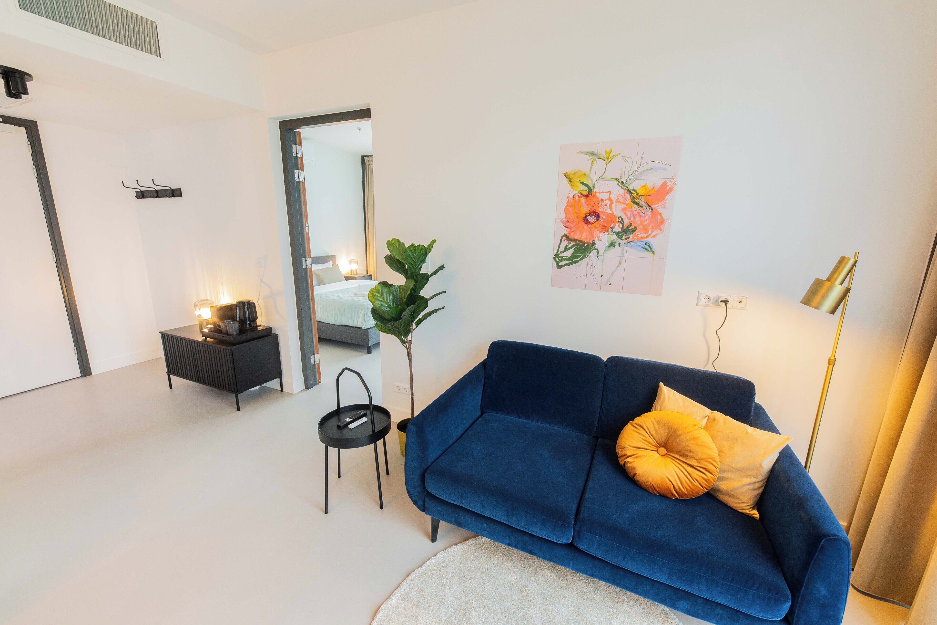 Una sala de estar moderna con un sofá azul, una mesita auxiliar, una planta en maceta y un cuadro en la pared.