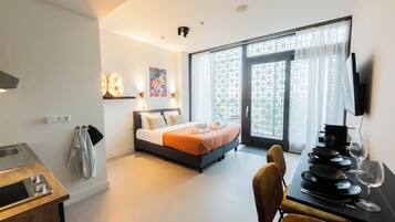 Una moderna camera d'albergo con un letto, un tavolo da pranzo con piatti e posate, una televisione e un'ampia finestra con tende.